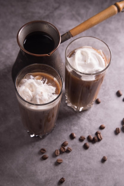 Caffettiera e due bicchieri di caffè freddo con panna montata su fondo scuro