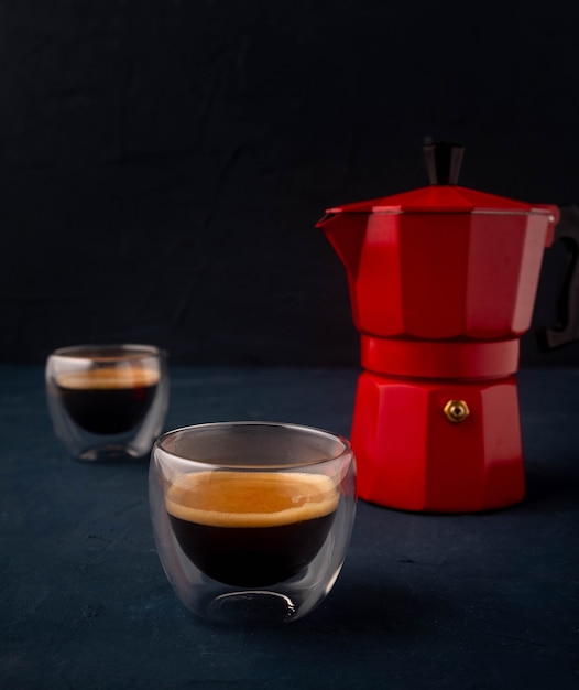 Caffettiera geyser e caffè in un bicchiere di vetro su un tavolo di legno sul nero.