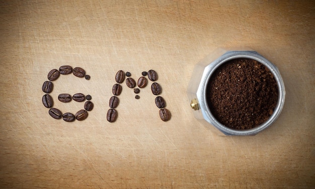 Caffettiera Mokka e un augurio con un buongiorno di chicchi di caffè su una tavola da cucina in legno