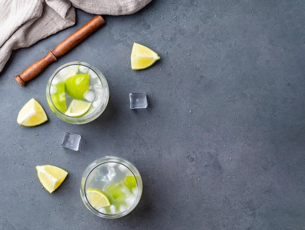 Caipirinha al limone brasiliano in bicchieri con fette di ghiaccio e frutta su sfondo di pietra con spazio per la copia