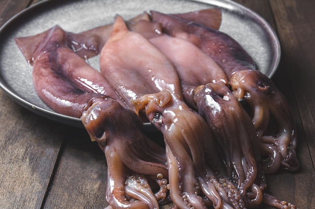 Calamari crudi su piastra grigia con coriandolo e limoni su fondo di legno scuro