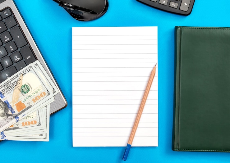 Foto calcolatore di soldi del libro del computer portatile del blocco note aperto in bianco e mouse del computer su una vista superiore blu