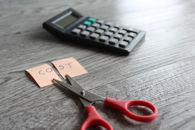 Calcolatrice a forbice e nota con testo COSTO Il taglio dei costi finanziari riduce il concetto di spese