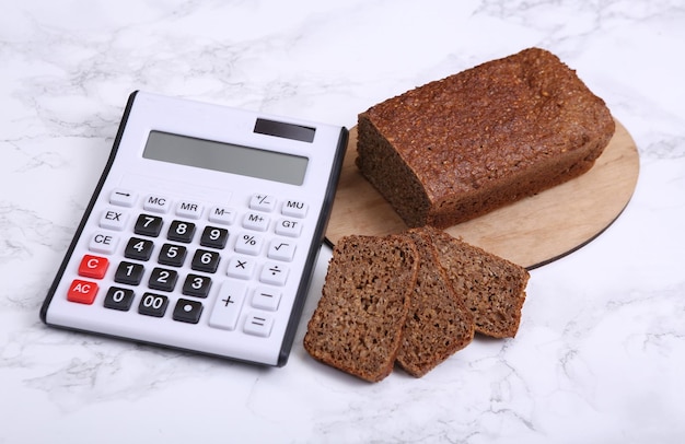 Calcolatrice con pane di segale integrale a fette su sfondo marmo Concetto di conteggio delle calorie della dieta