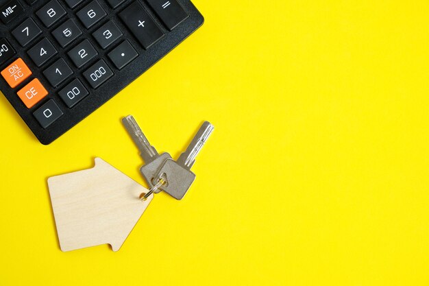 Calcolatrice e chiavi di casa concetto di acquisto e vendita di ipoteche abitative e affitto di una casa o di un appartamento sfondo giallo