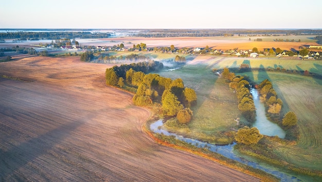 Calda mattina soleggiata di settembre autunno bellissimo paesaggio nebbioso piccole curve del fiume negli alberi luminoso soleggiato fiume nebbioso vista panoramica dell'alba rurale villaggio nei campi agricoli Europa Bielorussia