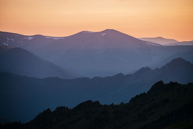 Calda sfumatura del cielo all'alba sopra strati di sagome di montagna e roccia. Vivace paesaggio alpino con montagne rocciose scure e cielo arancione alba. Scenario minimalista dell'altopiano con silhouette di montagne rocciose