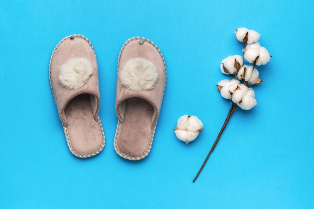 Calde pantofole e un rametto di cotone su sfondo azzurro Il concetto di scarpe da casa