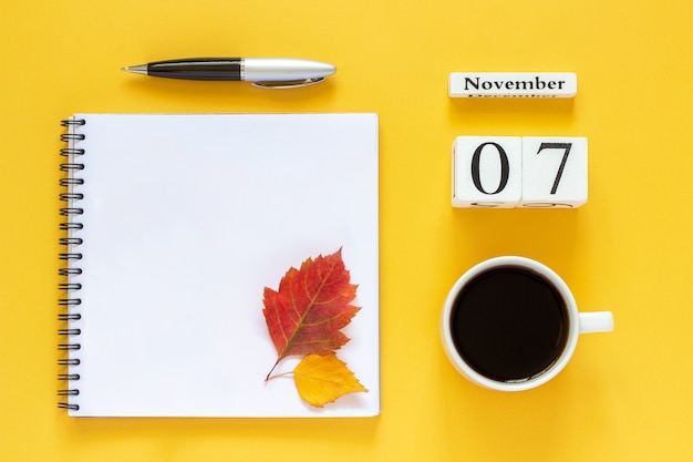 Calendario 07 novembre tazza di caffè, blocco note con penna e foglia gialla su sfondo giallo