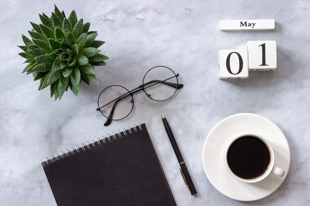 calendario 1 maggio. Notepad nero, tazza di caffè, succulente, occhiali Concept elegante posto di lavoro Flat lay