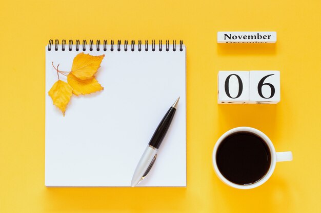 Calendario 6 novembre tazza di caffè, blocco note con penna e foglia gialla su superficie gialla