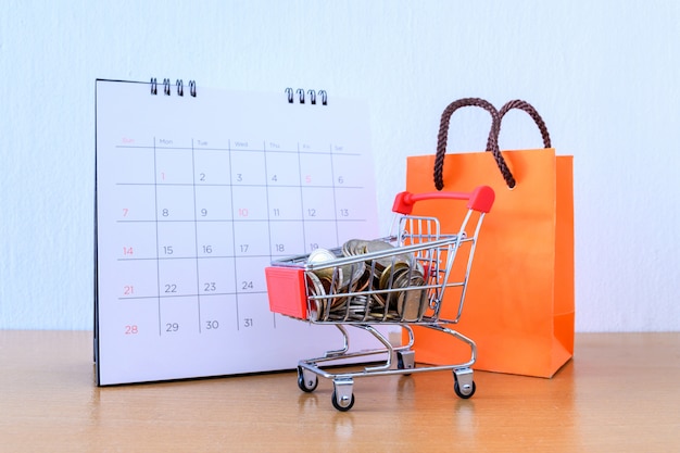 Calendario con giorni e carrello supermercato e sacco di carta arancione sul tavolo di legno. concetto di acquisto