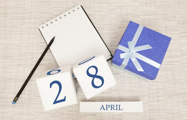 Calendario con testo blu e numeri alla moda per il 28 aprile e un regalo in una scatola.