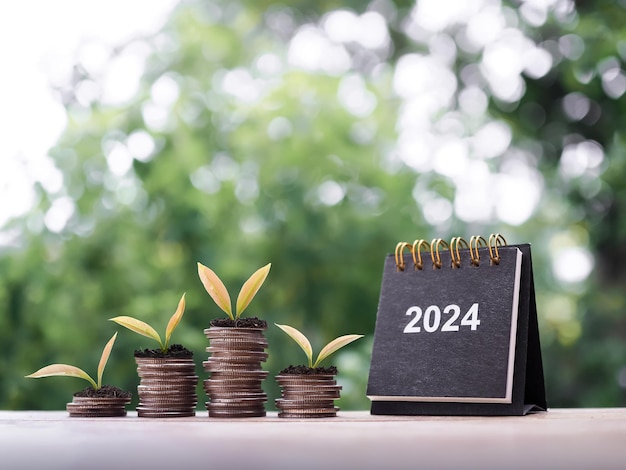 Calendario da tavolo 2024 Piante che crescono su una pila di monete Il concetto di risparmio di denaro Investimenti finanziari e affari in crescita nel nuovo anno 2024