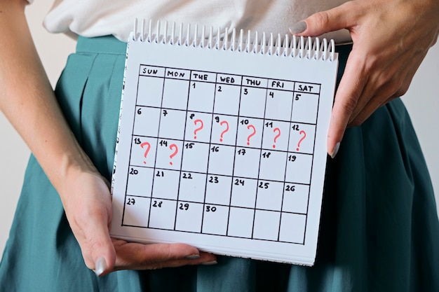 Calendario della holding della donna con il periodo mancato segnato. Gravidanza indesiderata, salute della donna e ritardo nelle mestruazioni.