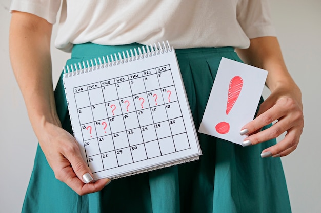 Calendario della tenuta della donna con il periodo e il punto esclamativo segnati mancati. Gravidanza indesiderata e ritardo nelle mestruazioni.