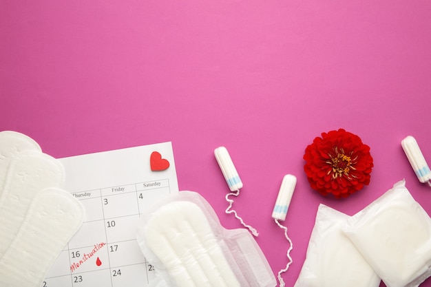 Calendario delle mestruazioni con tamponi di cotone e assorbenti con fiore su sfondo rosa. Giorni critici per la donna, protezione dell'igiene della donna. Dolore mestruale. Vista dall'alto