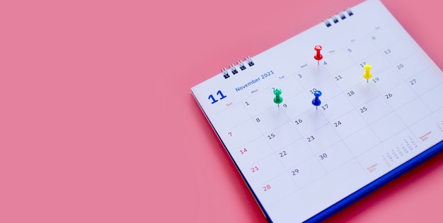 Calendario e pianificatore di appuntamenti con un perno su uno sfondo rosa.