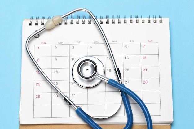 Calendario e stetoscopio su sfondo blu Il concetto di un esame pianificato da parte di un medico