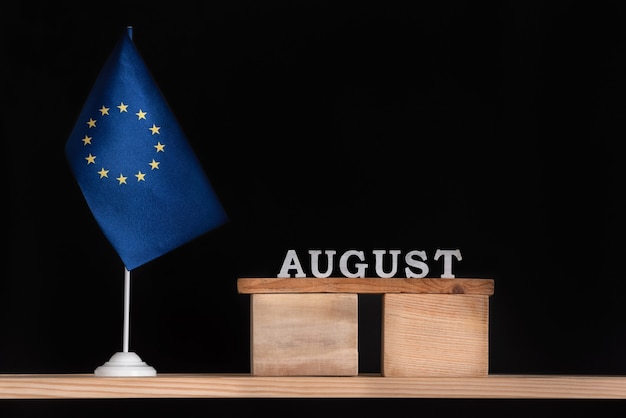 Calendario in legno di agosto con bandiera UE su sfondo nero. Vacanze dell'Unione Europea nel mese di agosto.