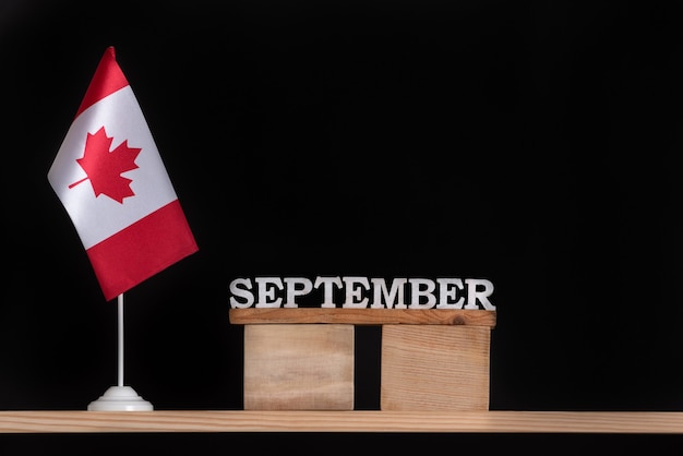 Calendario in legno di settembre con bandiera canadese su sfondo nero. Vacanze autunnali in Canada.