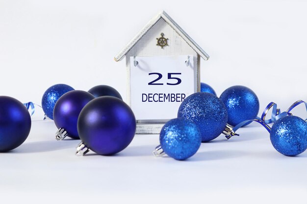 Calendario per il 25 dicembre una casa decorativa con il nome dicembre in inglese i numeri 25 tra i giocattoli di Natale blu uno sfondo chiaro