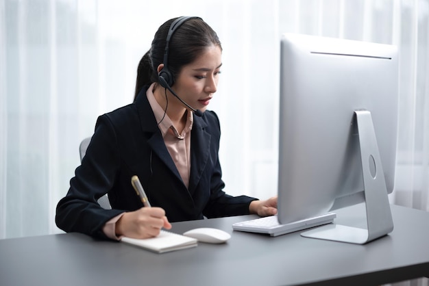 Call center asiatico entusiasta con cuffia e microfono che lavora sul suo laptop