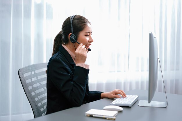 Call center asiatico entusiasta con cuffia e microfono che lavora sul suo laptop