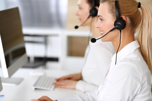 Call center Donna d'affari felice ed entusiasta che utilizza l'auricolare durante la consultazione dei clienti online Ufficio del servizio clienti o reparto di telemarketing Gruppo sorridente di operatori al lavoro