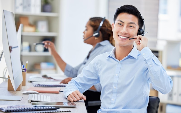 Call center ritratto e uomo asiatico sorridono per il telemarketing del servizio clienti o il supporto tecnico Face crm e consulente per agenti di vendita o coworking dipendente presso l'help desk ufficio aziendale e consulenza