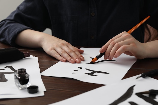 Calligrafia Donna con pennello e inchiostro che si esercita a scrivere i geroglifici cinesi su carta a un primo piano su un tavolo di legno