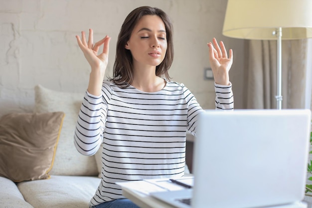 Calma bella donna che pratica yoga al lavoro meditando in ufficio a casa con gli occhi chiusi