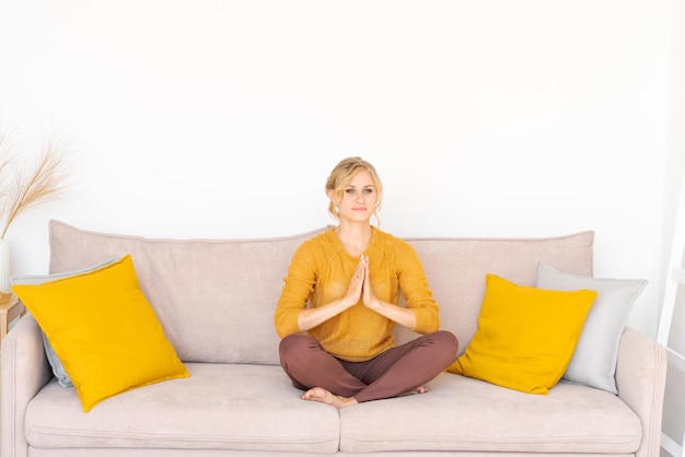 Calma donna caucasica seduta sul divano in soggiorno che pratica yoga alleviare