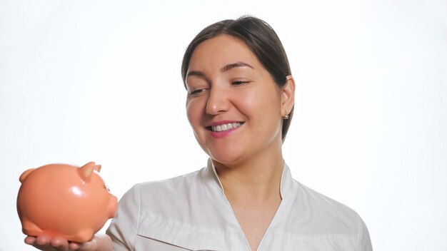 Calma donna dai capelli scuri tiene un piccolo salvadanaio rosa sul palmo