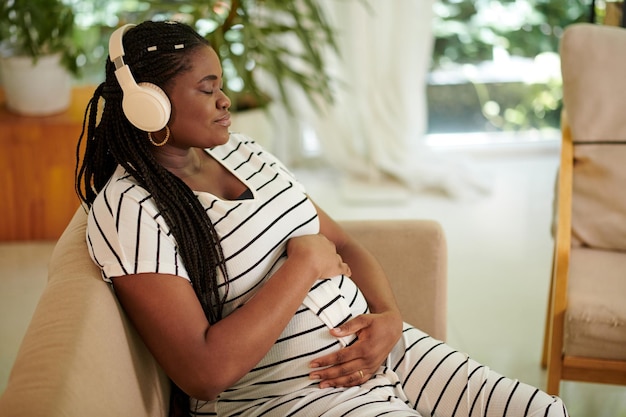 Calma donna nera che chiude gli occhi e ascolta musica di gravidanza per la madre e il feto