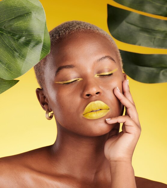 Calma donna nera trucco e bellezza naturale in relax per cosmetici con foglie contro uno sfondo giallo studio viso di persona femminile africana con gli occhi chiusi in soddisfazione per il trattamento facciale