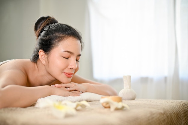 Calma giovane donna asiatica che si rilassa sul lettino da massaggio nella cura del corpo benessere del salone spa