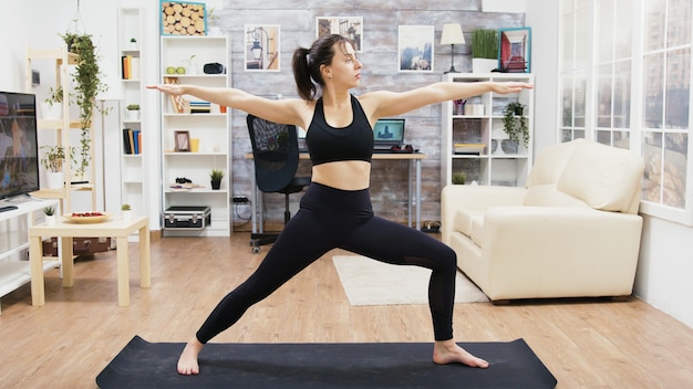 Calma giovane femmina che pratica esercizi di yoga nel soggiorno. Uno stile di vita sano.