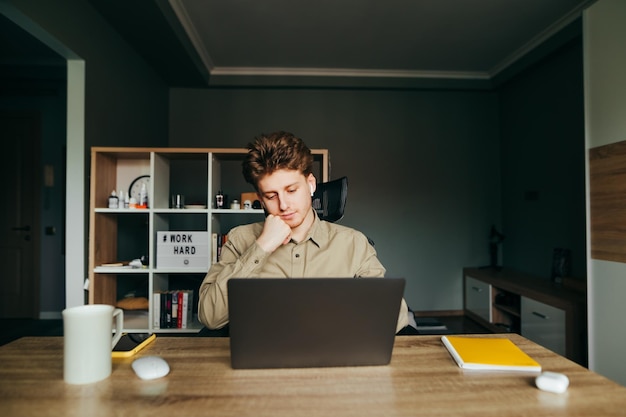 Calmo giovane libero professionista maschio in camicia che lavora al computer portatile in un'accogliente camera da letto a casa