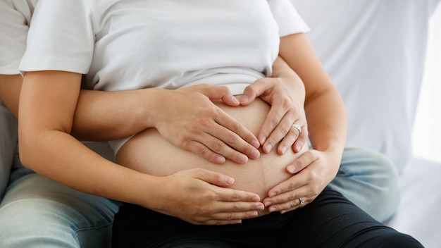 Calore adorabile concetto di famiglia. Immagine delle mani di un maschio e di una femmina che toccano la pancia di una donna incinta con amore e cura. Concentrati sulle mani di marito e moglie.