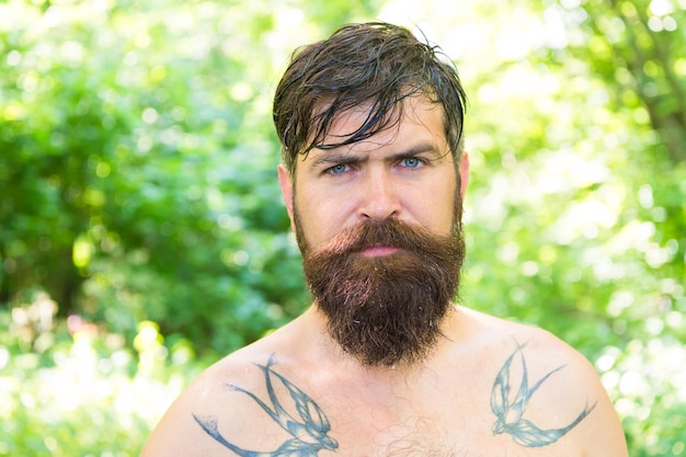 Calore estivo Ragazzo tatuato barbuto rilassarsi nella natura calda giornata estiva Hipster pelle bagnata e capelli sopravvivono al caldo Località di villeggiatura Calore estremo Uomo assetato hipster sudato nudo nella foresta Concetto di calore