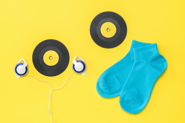 Calze sportive blu, cuffie e dischi in vinile su sfondo giallo. Il concetto di musica e sport. Disposizione piatta.