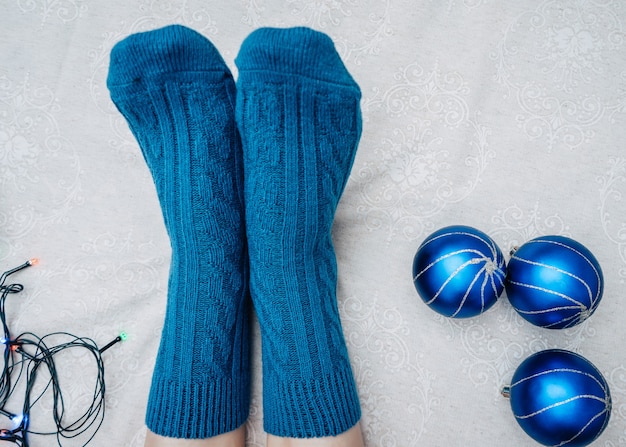 Calzini lavorati a maglia blu sui piedi con palle di natale e luci natalizie