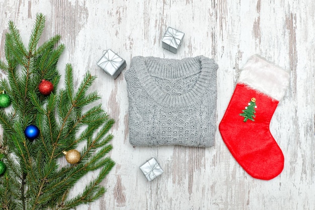 Calzino di Natale rosso e un maglione grigio Ramo di abete decorato Fondo in legno Concetto alla moda