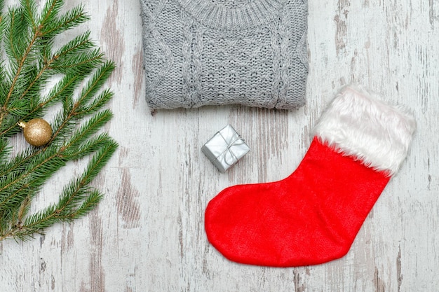 Calzino di Natale rosso e un maglione grigio Ramo di abete decorato Fondo in legno Concetto alla moda