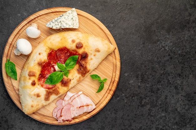 Calzone con prosciutto e funghi su uno sfondo di pietra con copia spazio per il tuo testo