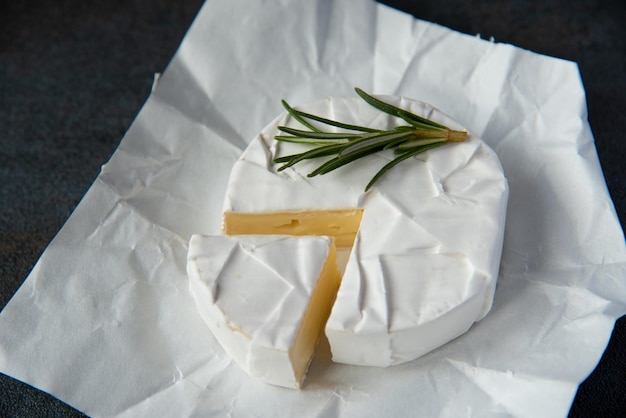 Camembert al formaggio o brie con rosmarino e pepe su fondo di pietra scuro. Copia spazio. Foto in studio.