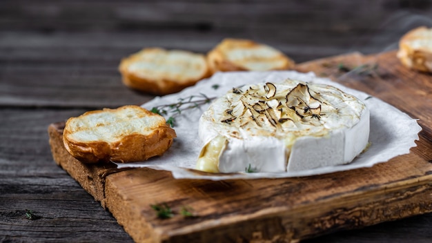 Camembert al forno caldo delizioso con timo e pane baguette sulla tavola di legno.