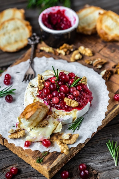 Camembert al forno casalingo francese tradizionale con toast, rosmarino, mirtilli rossi e noci sulla tavola di legno rustica.