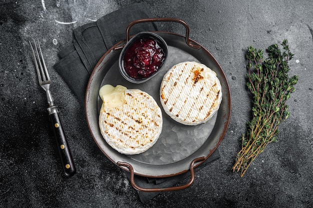 Camembert al forno su un vassoio d'acciaio con salsa di mirtilli rossi e timo Sfondo nero Vista dall'alto